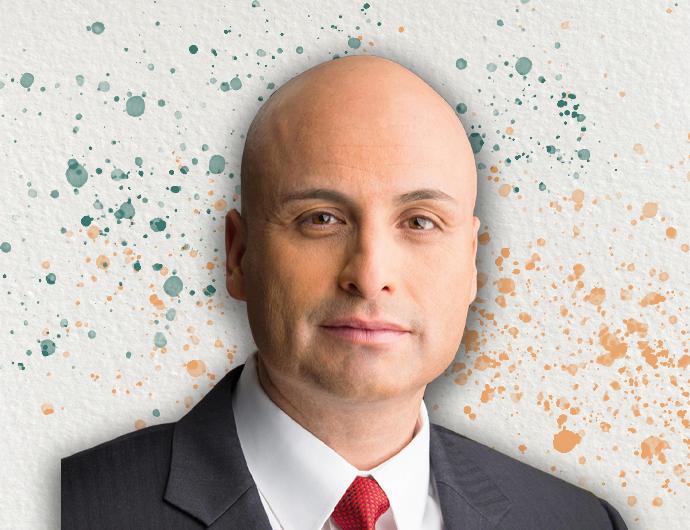 Headshot of AG Balderas in a grey suit with red tie, overtop an off-white background with green and orange spatter