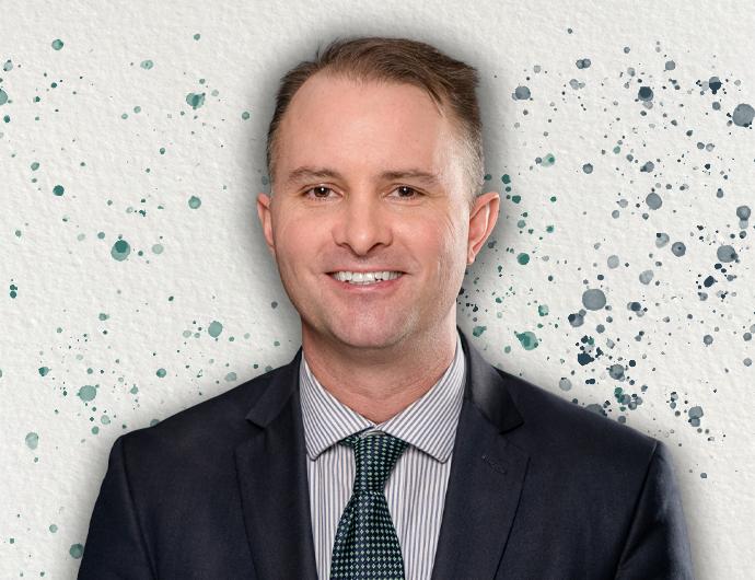 Headshot of AG TJ Donovan in a black suit with green tie, over an off-white background with green and blue spatter