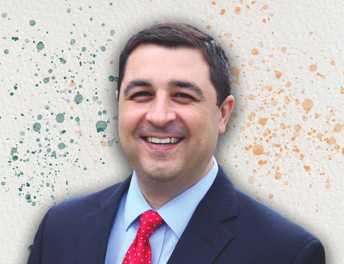 Headshot of AG Josh Kaul in a navy suit with red tie, overtop an off-white background with green and orange spatter