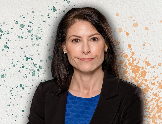 Headshot of AG Dana Nessel in a black suit with blue blouse, overtop an off-white background with green and orange spatter