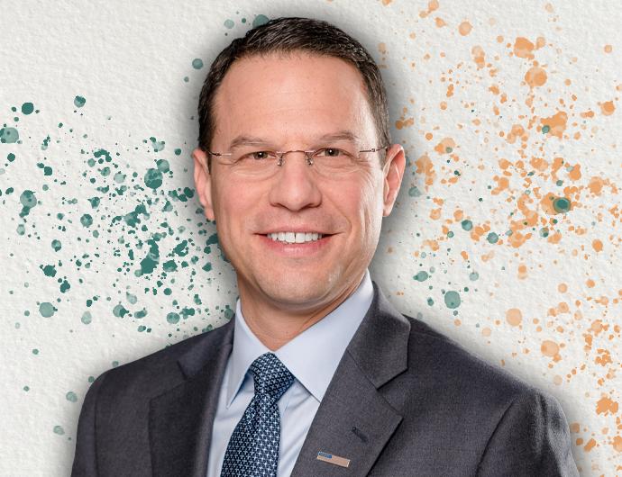 Headshot of AG Josh Shapiro in a grey suit and navy tie, overtop an off-white background with green and orange spatter